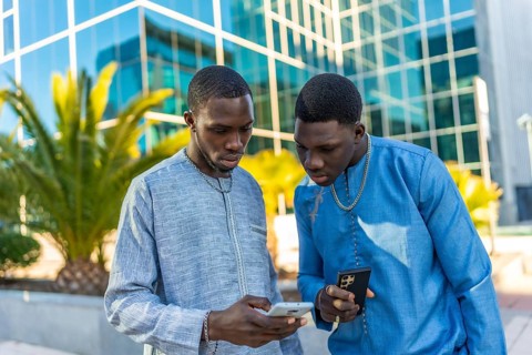 Two senegalese businessmen in traditional dashiki attire using smartphones in front of a modern