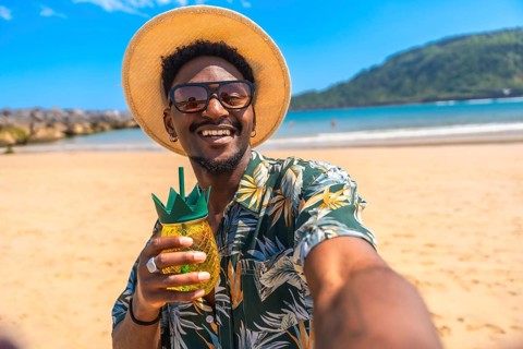 Young man taking a selfie while holding a tropical cocktail in a pineapple shaped glass on a sunny