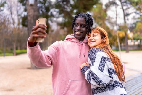 Young multiracial couple taking a selfie with a smartphone in a park, smiling and hugging