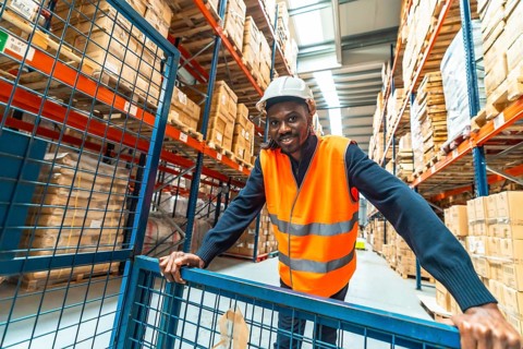View from inside a cart of a happy african worker pushing trolley in a distribution warehouse