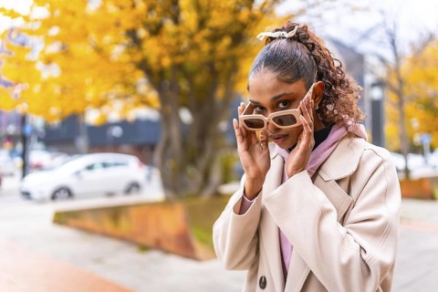 Flirty young african woman with sunglasses and coat in the city in a cold day of autumn