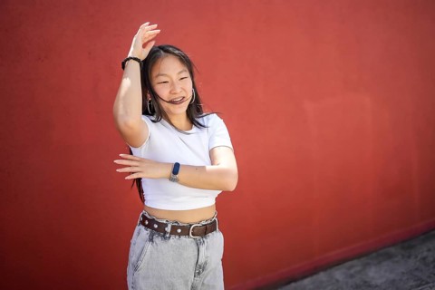 Happy energetic asian woman raising arms choreographing a urban dance outdoors against a red wall