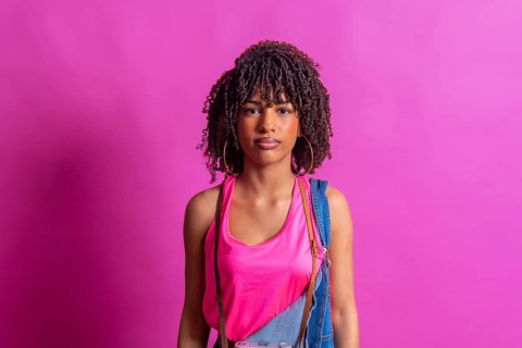 Young woman photographer with curly hair posing with vintage camera on pink background,