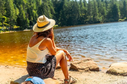 Woman tourist with hat sitting in the landscape at Mummel Lake or mummelsee, Black Forest of