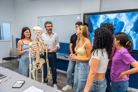 Professor demonstrates human anatomy with a skeleton model and x ray display while a diverse group
