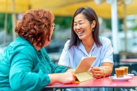 Woman with disability and multi-ethnic friend talking using digital tablet in a sidewalk outdoors