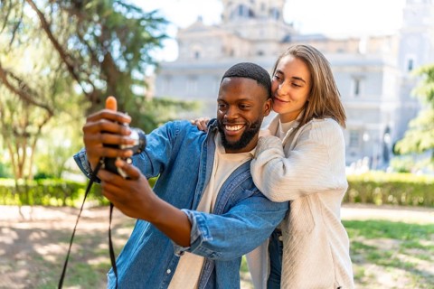 Multiracial couple taking selfie with camera in a park with city views