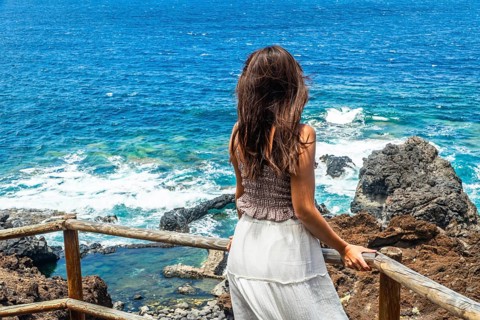 Woman looking out at the deep blue ocean and rugged volcanic coastline from a wooden walkway,