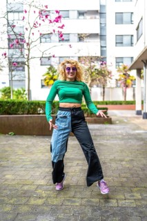Young caucasian woman with curly blonde hair, green top and two tone pants dancing in the city
