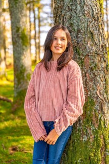 Vertical three quarter length photo of a caucasian Girl leaning relaxed on a tree trunk in the