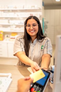 Vertical photo of a smiling pharmacist attending a client while paying with credit card in the