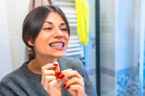 Adult caucasian beauty woman looking at the mirror wearing transparent dental aligner in the