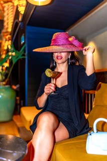 Vertical photo of a woman wearing elegant clothes and hat sitting drinking luxury cocktail in a
