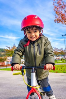 A young boy is riding a bike with a red helmet on. He is smiling and he is enjoying himself