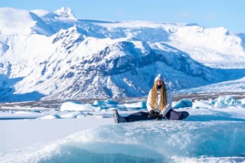 Woman sitting smiling sitting on the ice of Jokulsarlon lake on her vacation in Iceland