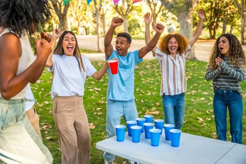 Happy multi-ethnic friends raising arms celebrating an score while playing beer pong in a park