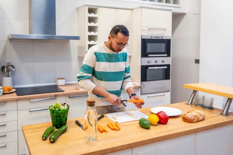 Man peeling a carrot on a cutting board, preparing fresh vegetables for a meal in a modern kitchen,