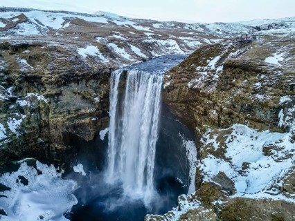 Drone aerial view of Skogafoss waterfall with snow and lots of water in winter in Iceland