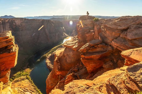 Person standing on a rock cliff looking at the majestic horseshoe bend of the colorado river,