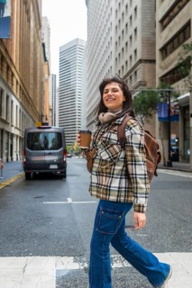 Young woman smiling while walking across a san francisco city street, holding a disposable coffee