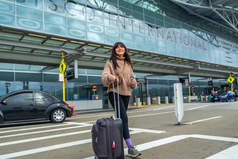Young woman smiling and pulling luggage, walking from the international terminal building at san