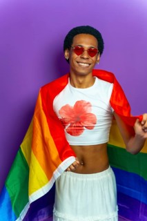 Studio portrait with purple background of a latin gay man wrapped in lgtb flag