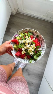 Person holding a bowl of refreshing watermelon and feta salad with cucumber, red onion, and mint,