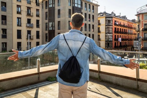 Man with backpack standing on a terrace with arms outstretched, experiencing freedom and success