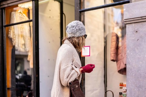 Young Caucasian blonde girl shopping in the city in winter, looking at clothing stores. Sunglasses