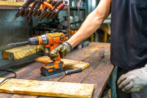 Close-up of a worker wearing protective gloves using an electric drill in a factory