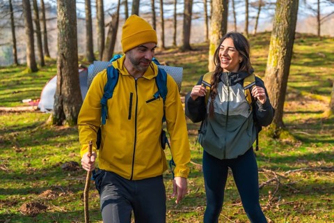 Happy hikers walking in forest, carrying backpacks and using hiking poles, enjoying nature near
