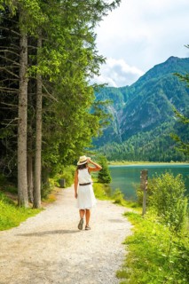 Tourist walking along a gravel path by lake dobbiaco with mountains and pine forest in the
