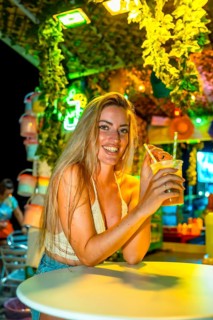 Vertical photo of a blonde woman drinking cocktail enjoying summer night