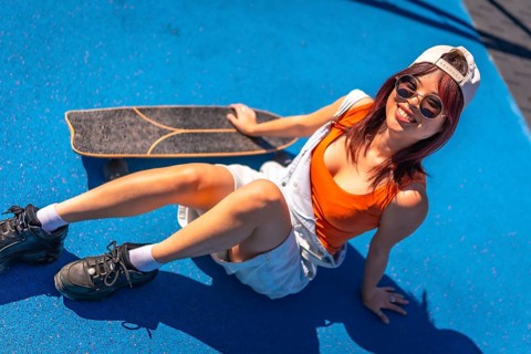Top view of a cool urban woman with sunglasses and cap sitting with her skateboard in a colorful