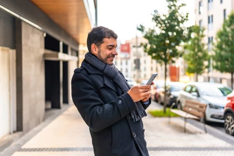 Side view of a happy casual businessman with winter clothes smiling using phone in the city