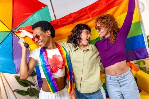 Multi-ethnic friends waving lgbt rainbow flag and dancing partying at home and celebrating pride