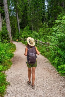 Woman with backpack walking on path in forest near lake carezza, dolomites, italy, on a summer day