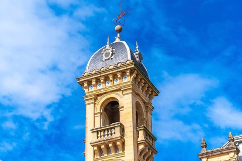 Elegant clock tower with intricate architectural details stands tall under a bright blue sky,