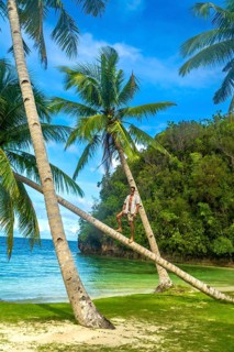 Young man standing on leaning palm trees on a beautiful tropical beach in kangbangyo island,