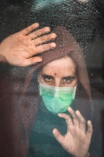 Sad look of a young man with a mask in the Covid-19 pandemic looking through a window