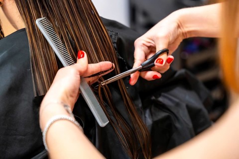 Professional hairdresser's hands with red polished nails holding a comb and scissors, carefully