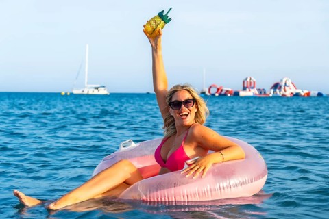 Blonde woman celebrating her summer vacation, sitting on a pink inflatable ring while holding a