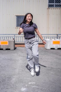 Vertical photo of a female happy young urban korean dancer jumping energetically performing in an