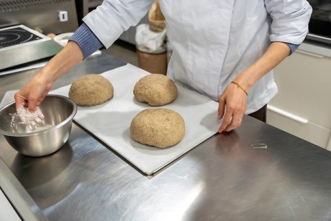 Chef hands preparing three rounded bread dough portions on a baking sheet, with one hand dipping
