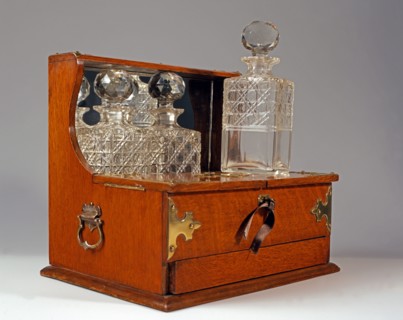 Tantalus en chêne avec trois bouteilles de cristal gravé.