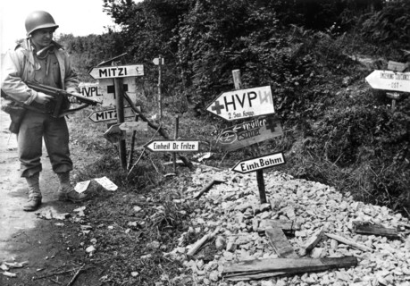 Soldat américain devant les panneaux placés par les Allemands en Normandie, juillet 1944