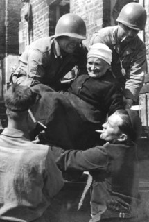 Les soldats américains apportent leur aide à une femme âgée, dans la région de Tessy-sur-Vire.
(Août 1944)