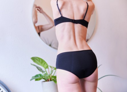 A woman wears period underwear while standing in front of a mirror in a room. (posed scene) Period