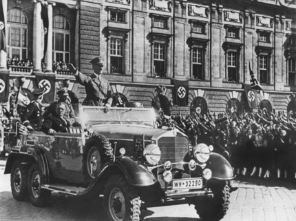 Adolf Hitler grüßt die ihm zujubelnde Menschenmenge in Wien stehend in einem Auto, sitzend neben
