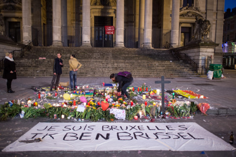 A man lights a candle behind a banner that reads 'Je suis Bruxelles Ik ben Brussel' (lit. I am